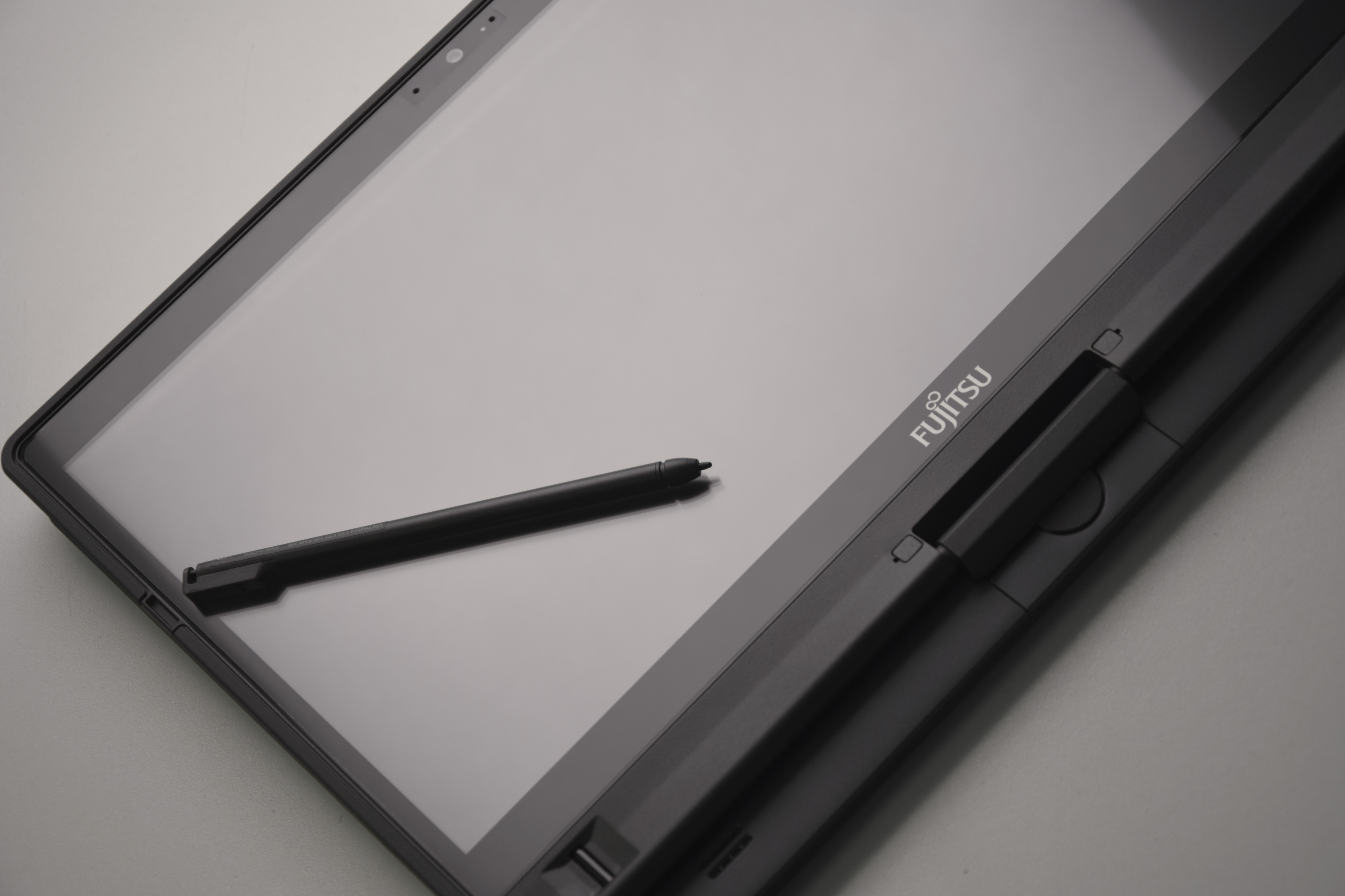 Tablet Fujitsu Lifebook T937 z czarnym rysikiem leżącym na ekranie, widok z ukosa na logo i przyciski obudowy