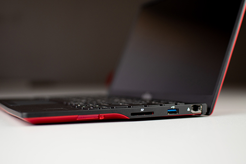 Bok laptopa Fujitsu z czerwonym wykończeniem, widoczne porty USB 3.0, czytnik kart i gniazdo sieciowe.